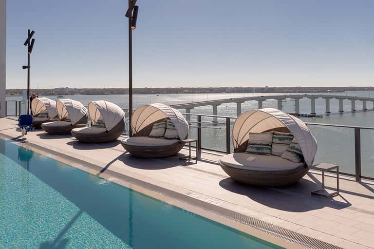 Resort rooftop lounge with canopied daybed chairs overlooking a bay and bridge spanning the water