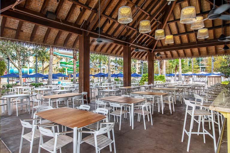 Open-air dining pavilion with wooden beam ceiling, woven pendant lights, and white contemporary furniture