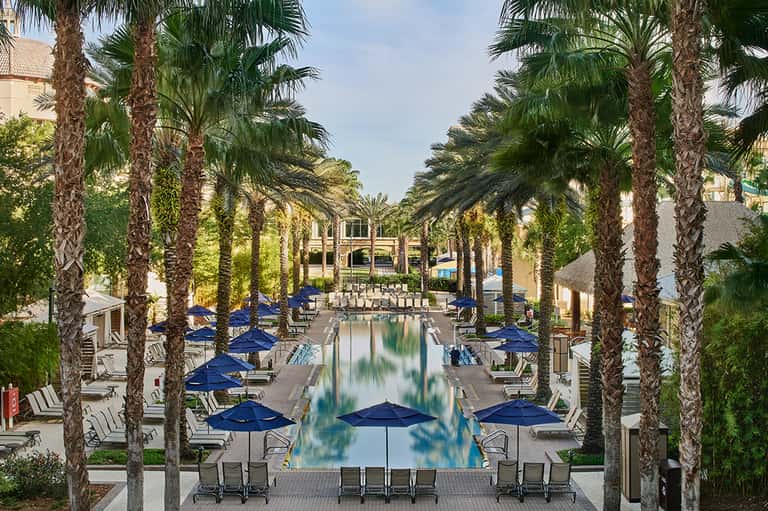 Luxurious resort pool lined with blue umbrellas and palm trees, reflecting in still water