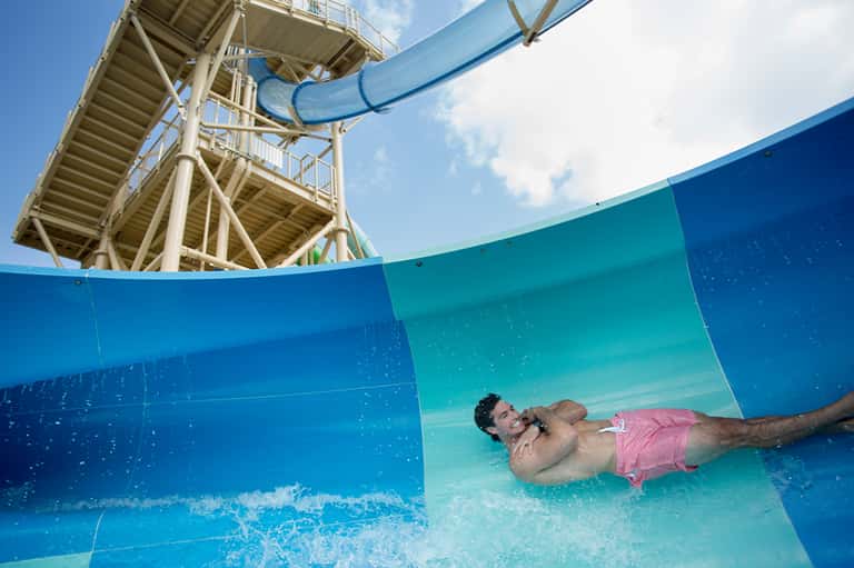 Man sliding down blue water slide into shallow pool area
