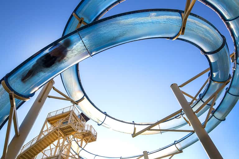 Blue water slides against clear sky with support structure and viewing platform at waterpark