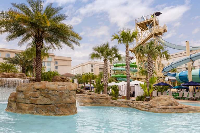 Outdoor water park with turquoise pools, palm trees, water slides, and sandy beach area