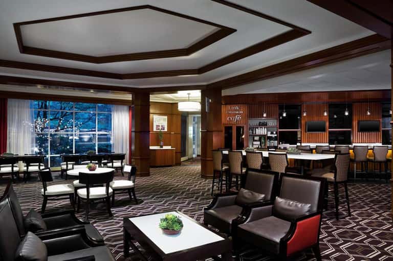Upscale hotel lounge with dark wood ceiling, leather seating, bar area, and panoramic windows