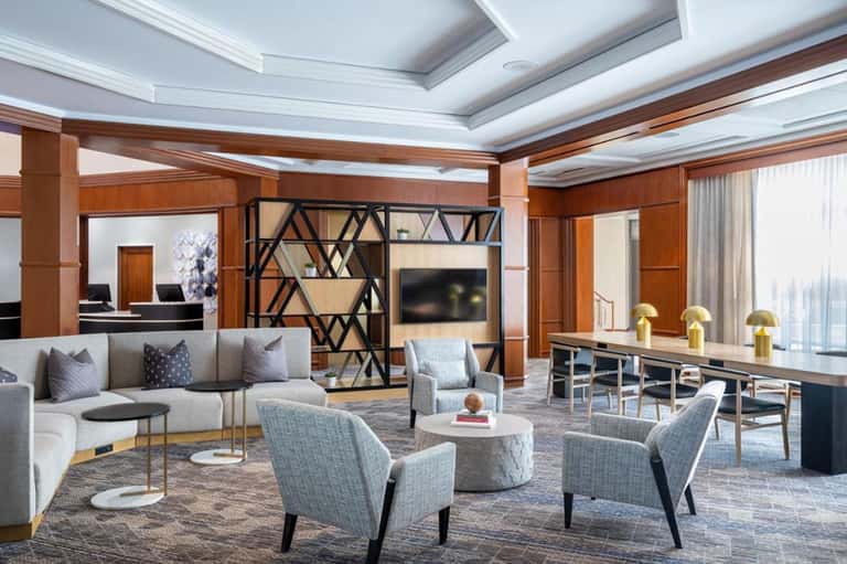 Luxury hotel suite lounge with coffered ceiling, gray sectional sofa, modern fireplace divider, and dining area