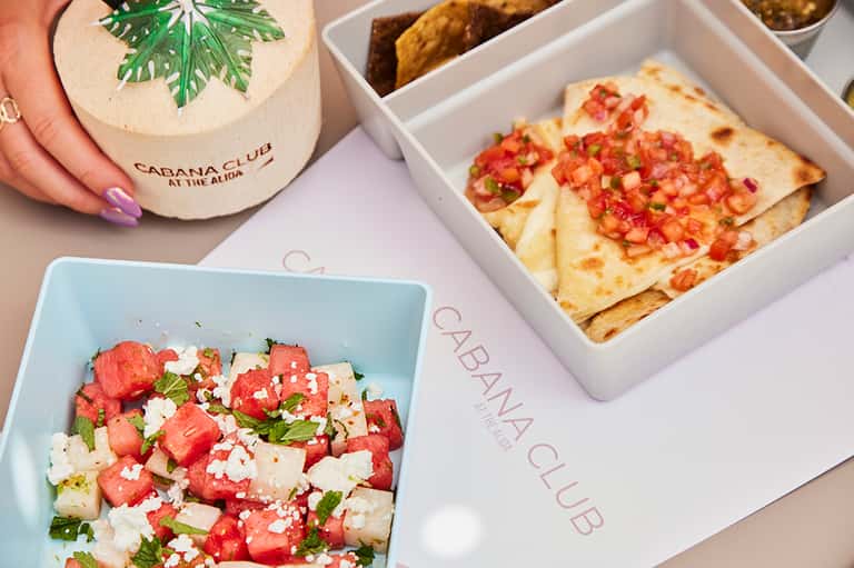 Cabana Club appetizers including watermelon salad, flatbread pizza, and fried tortilla chips on white serving dishes