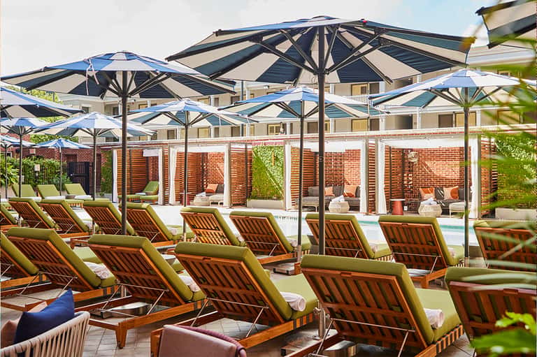 Outdoor lounge area with striped chairs under large umbrellas beside a brick wall