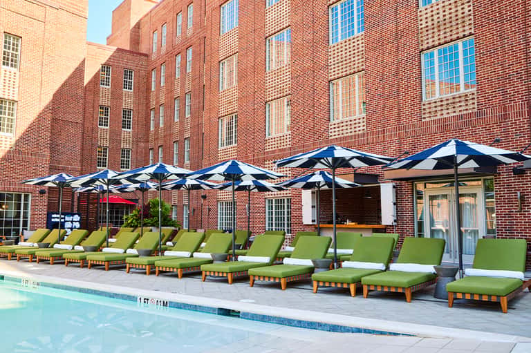 Brick courtyard pool area with lime-green lounge chairs, blue and white striped umbrellas, and historic brick buildings