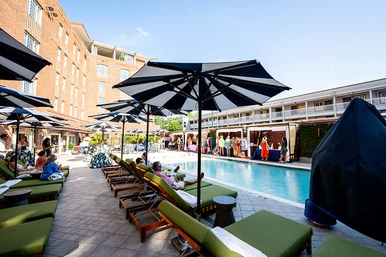Courtyard pool area with black umbrellas, green lounge chairs, and brick hotel buildings surrounding the space
