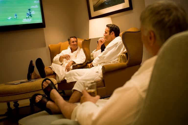Three men in white robes relaxing in lounge chairs watching a football game on TV