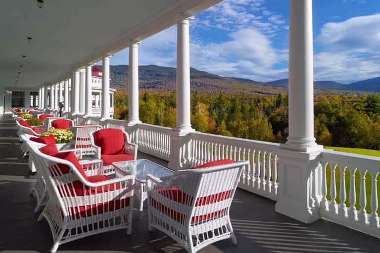 Mountain view from white columned porch with red cushioned wicker chairs and autumn forest