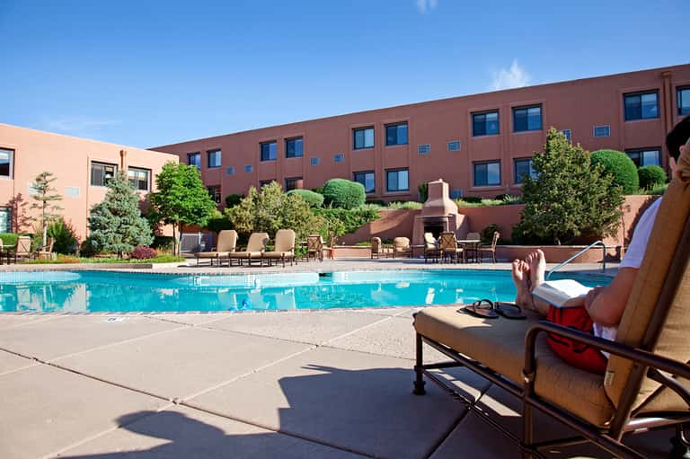 Resort guest relaxing on lounge chair by rectangular pool with red brick building and landscaping
