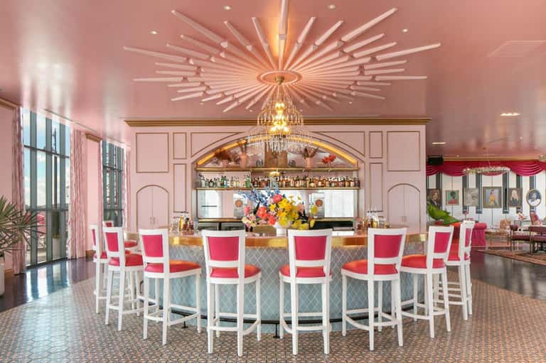Elegant pink bar with white chairs, crystal chandelier, and colorful floral arrangement