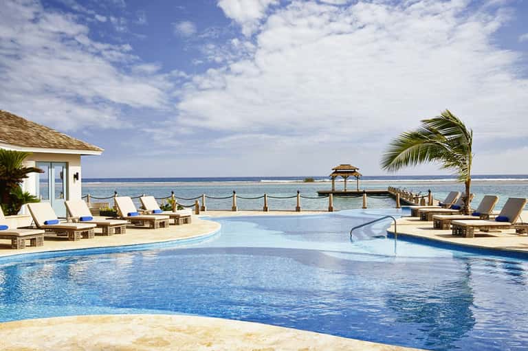 Oceanfront infinity pool with lounge chairs, gazebo, and pristine Caribbean waters under blue sky