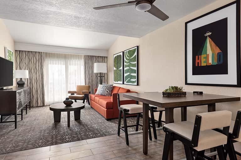 Modern hotel suite with orange sofa, dining table, and contemporary artwork on beige walls