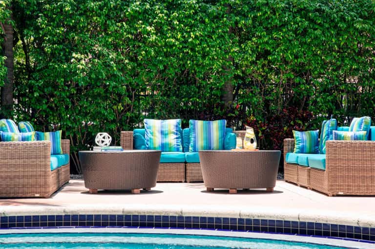 Woven lounge chairs with striped blue cushions arranged poolside behind a sparkling blue pool with lush green foliage backdrop