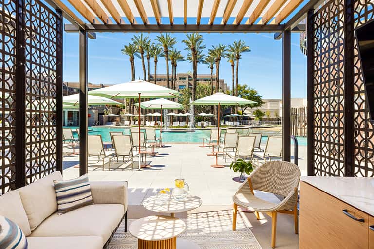 Modern poolside lounge area with white umbrellas, palm trees, and geometric shade screens