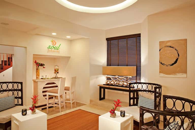 Modern spa lounge with beige walls, black geometric furniture, wooden accents, and decorative artwork