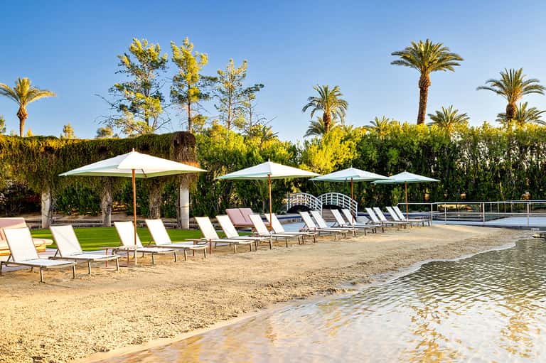 Beach resort with white umbrellas, lounge chairs, palm trees, and calm shallow water