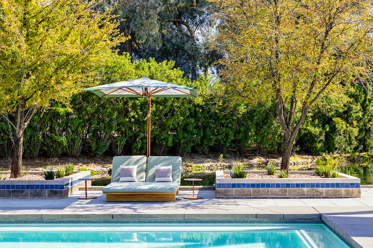 Modern poolside lounge with umbrella and cushioned seating surrounded by trees