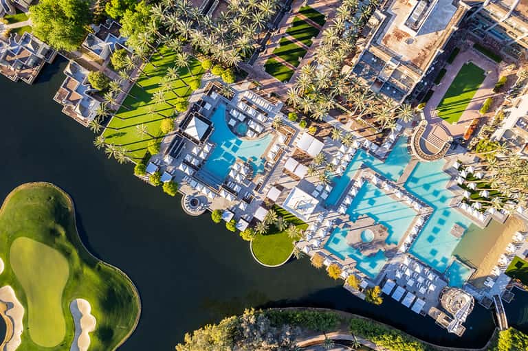 Aerial view of luxury resort with multiple pools, palm trees, and waterfront location