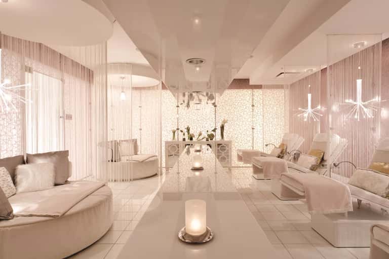 Luxurious spa lounge with pink tones, curved seating, decorative screens, and hanging crystal light fixtures