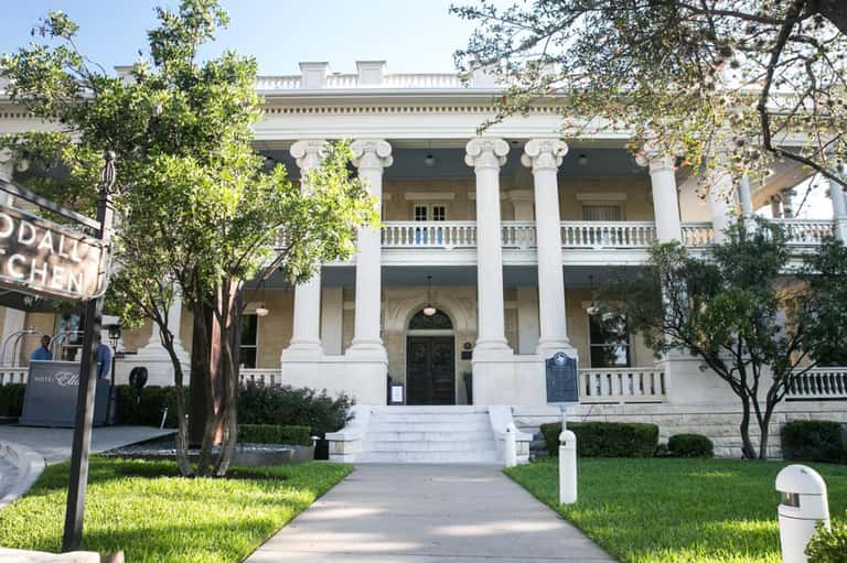 Historic white columned mansion with neoclassical architecture, manicured gardens, and brick pathway entrance
