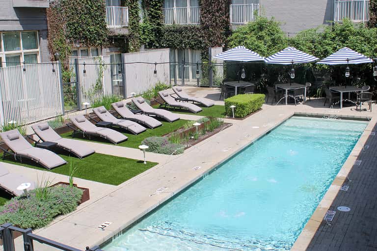 Resort pool deck with loungers, blue striped umbrellas, dining area, and ivy-covered building facade