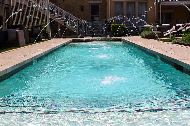 Rectangular swimming pool with decorative fountains, brick courtyard, and residential building