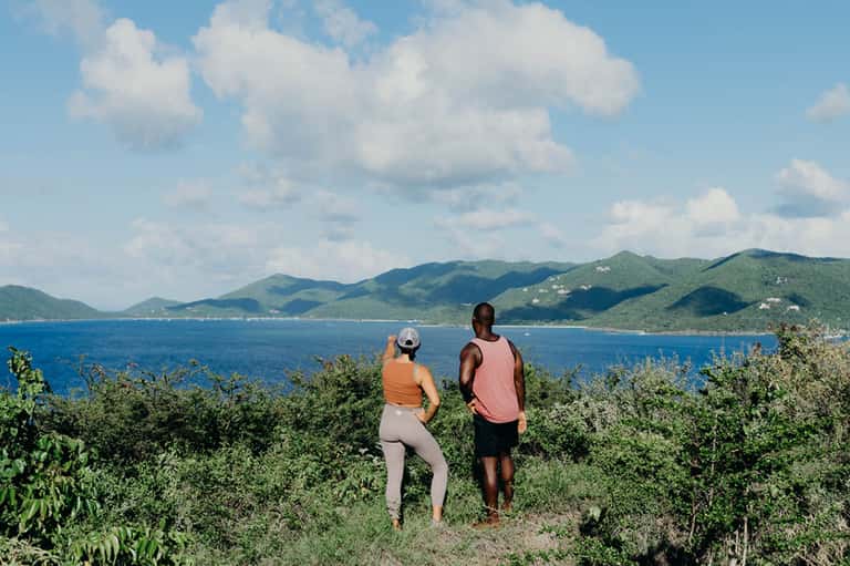 Two runners jogging on a coastal trail overlooking a blue bay with green mountains