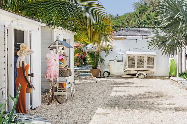 Beachside resort courtyard with white cottages, vintage airstream trailer, palm trees, and sandy grounds