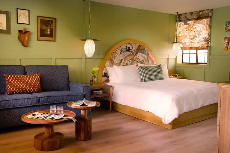 Modern hotel bedroom with lime green walls, wooden headboard, and lounge area