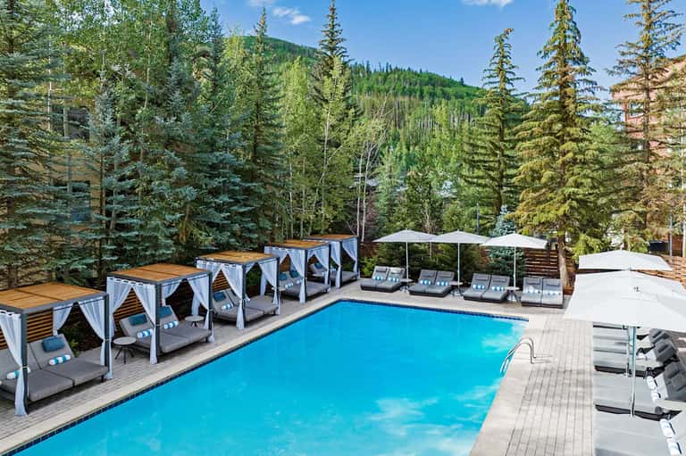 Resort pool with cabanas surrounded by evergreen forest and mountain landscape