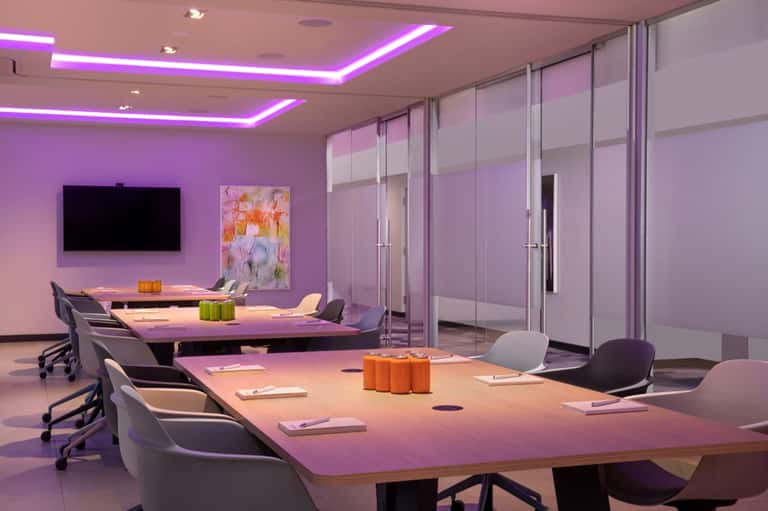 Modern conference room with purple ambient lighting, glass partitions, and long dining tables with orange accents