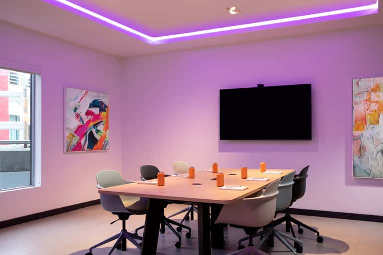 Modern conference room with purple accent walls, neon ceiling lighting, meeting table, and pop art wall decor