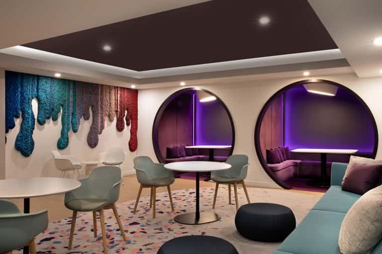 Modern lounge with purple neon-lit pod seating, colorful wall art, and contemporary furniture in soft tones