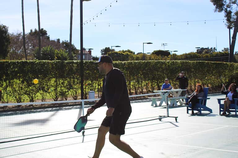 Man playing pickleball on outdoor court with vineyard views and spectators in background