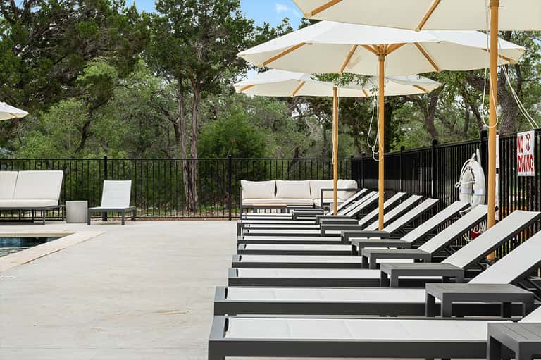 Resort pool deck with lounge chairs and cream umbrellas overlooking forested landscape