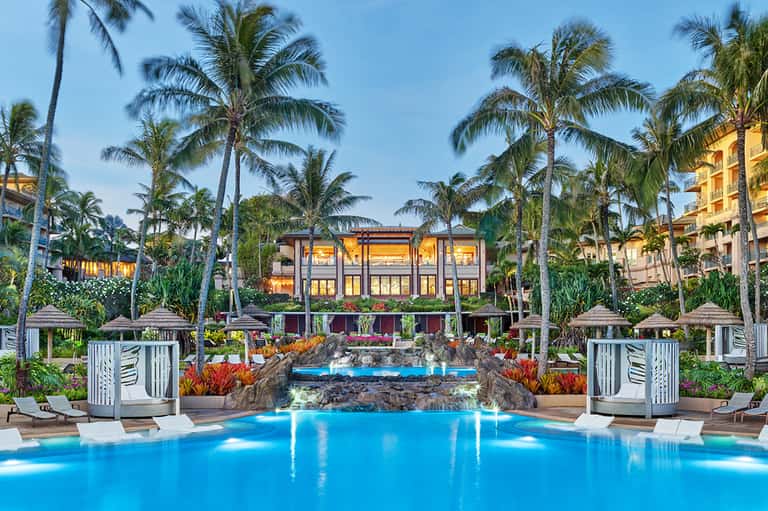 Luxury resort pool with tropical palm trees, lounge chairs, and illuminated building at dusk