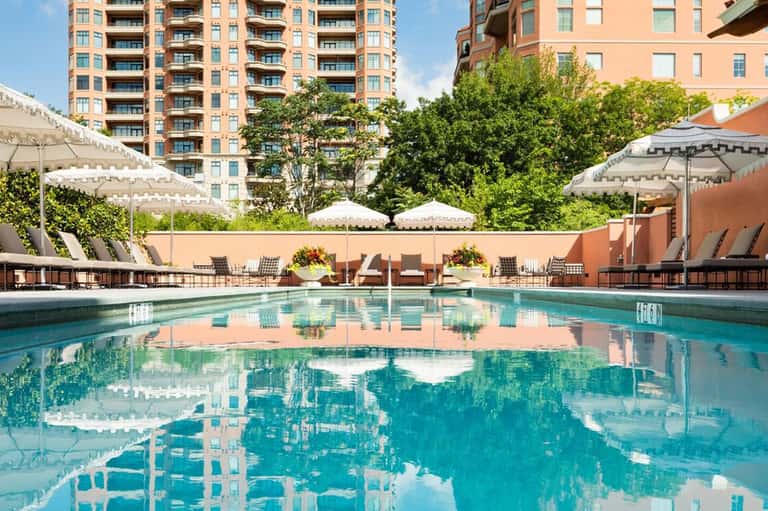 Resort outdoor pool with lounge chairs, white umbrellas, and high-rise buildings in background