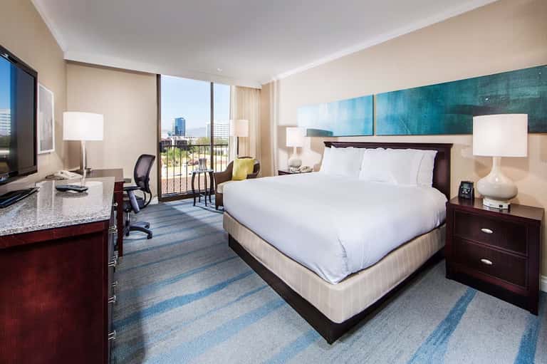 Upscale hotel room with king bed, work desk, and balcony overlooking cityscape