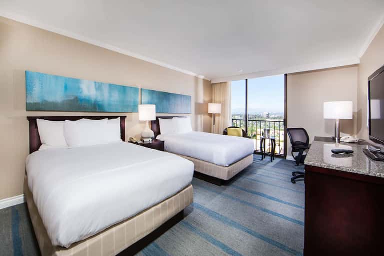Modern hotel room with two queen beds, city skyline view, work desk, and contemporary furnishings