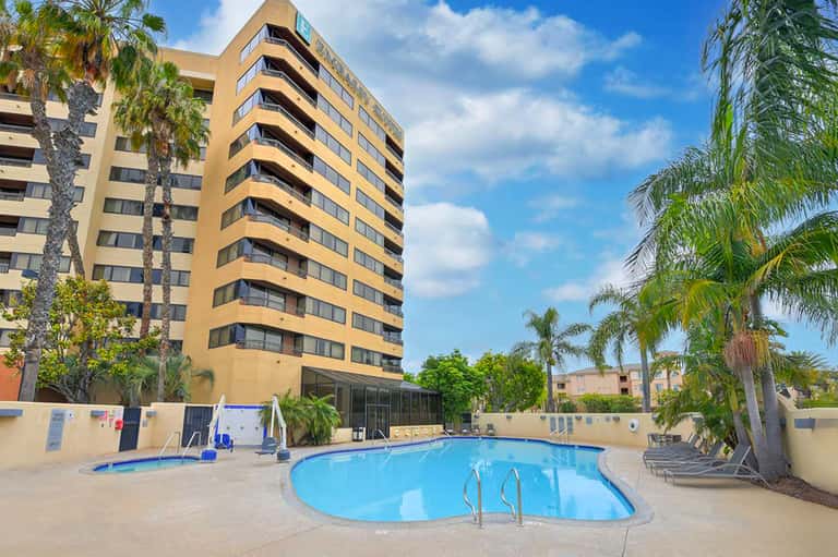Yellow apartment building with kidney-shaped pool and lounge chairs in courtyard