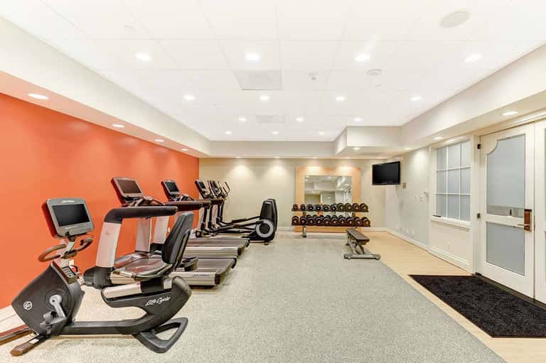 Modern fitness center with orange accent wall, cardio equipment, treadmills, stationary bikes, dumbbells, and mirrors