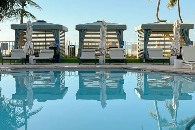 Luxury poolside cabanas with teal canopies and loungers reflected in crystal-clear water