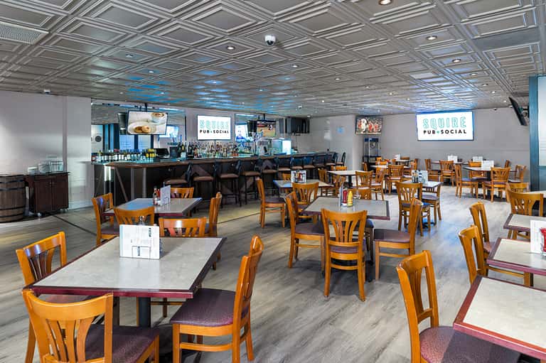 Indoor pub-social space with wooden chairs, tables, bar counter, and blue ceiling accents