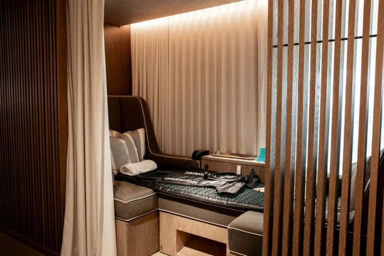 Modern hotel pod bed with wood slat partition, cream curtains, and built-in storage in minimalist room design
