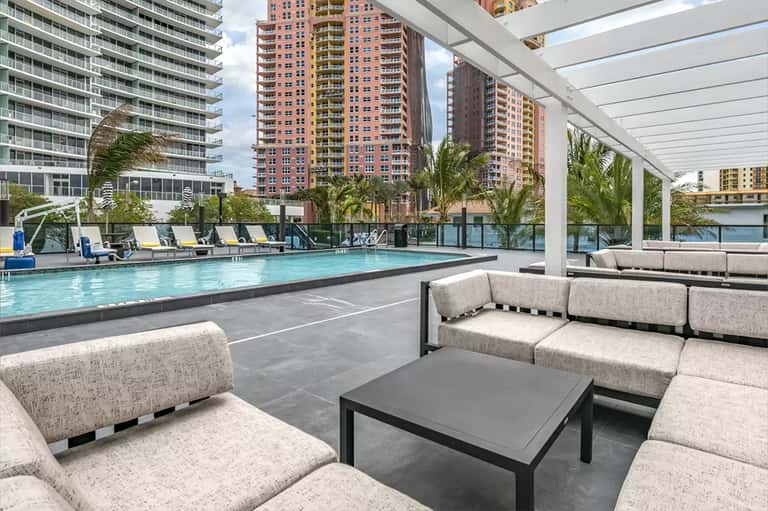 Rooftop pool deck with lounge seating, white pergola, and cityscape views of tall buildings