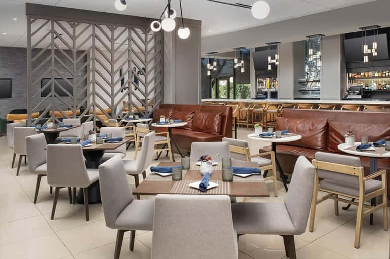 Modern restaurant dining area with geometric wood dividers, brown leather booths, gray upholstered chairs, and pendant lighting