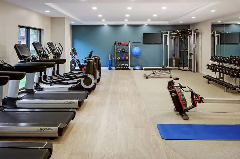 Modern fitness center with treadmills, ellipticals, weights, and exercise equipment on light wood flooring