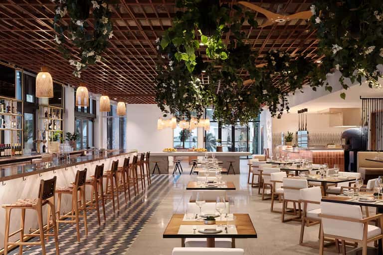 Modern restaurant interior with wooden lattice ceiling, green plants, and dining tables